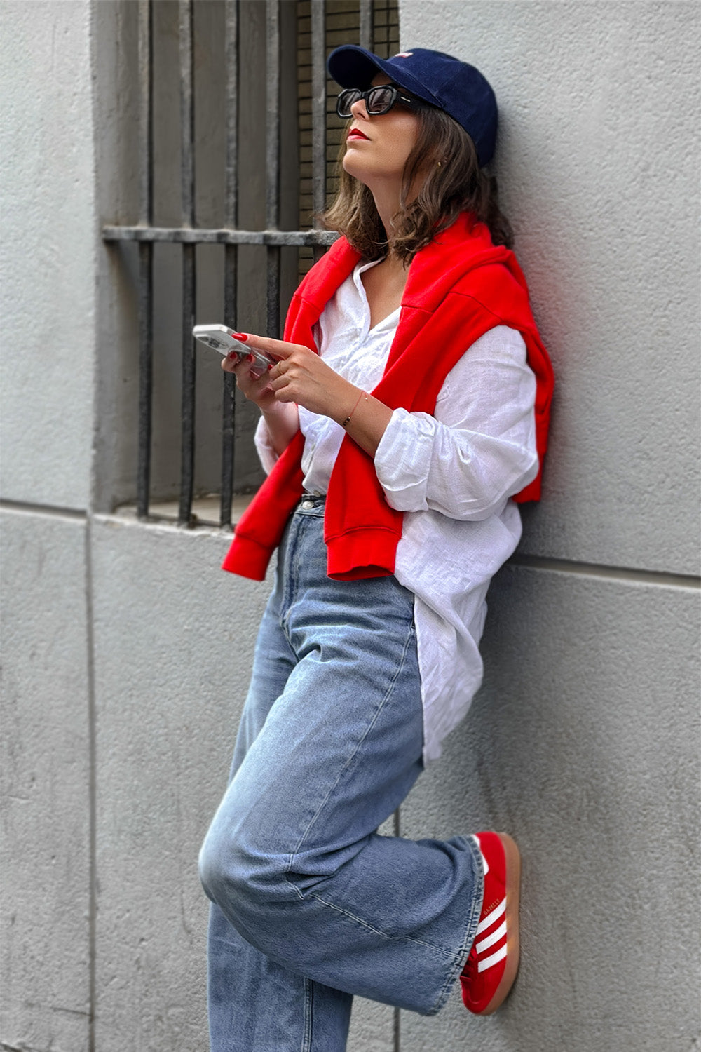 Una mujer apoyada contra una pared revisa su celular.